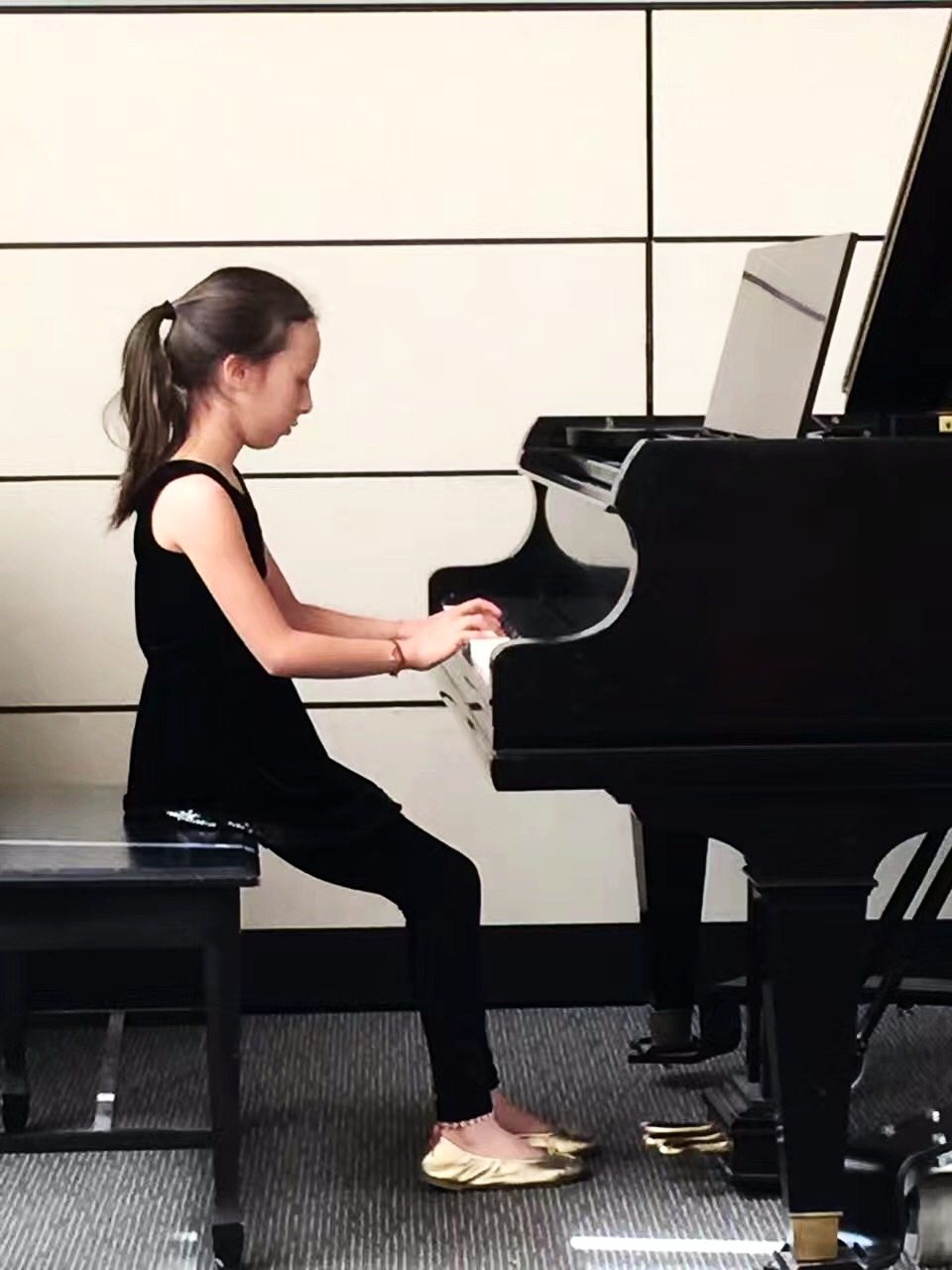 A young child learning piano beside a teacher in a bright music room