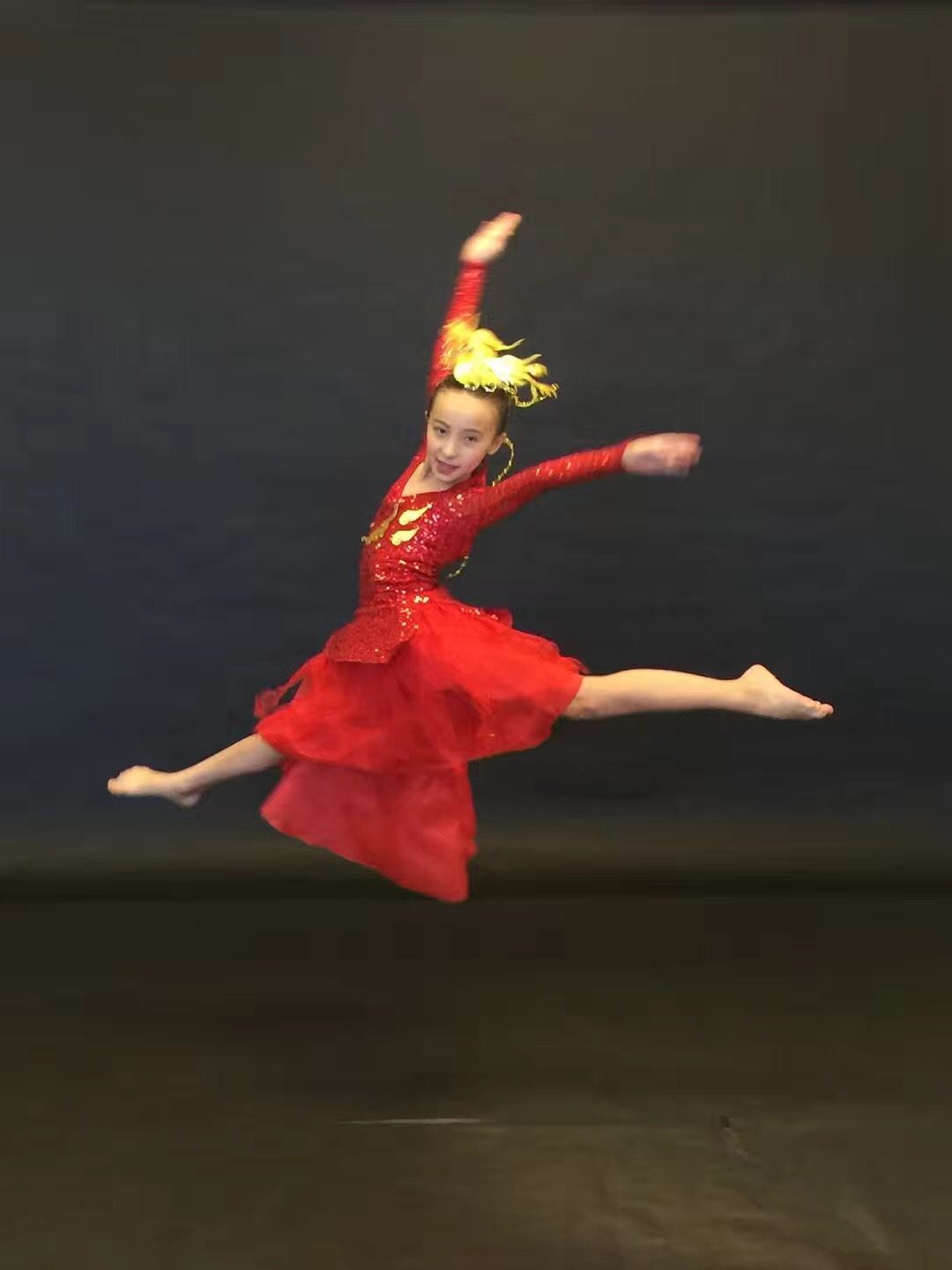 A dance student mid-leap in a red performance costume